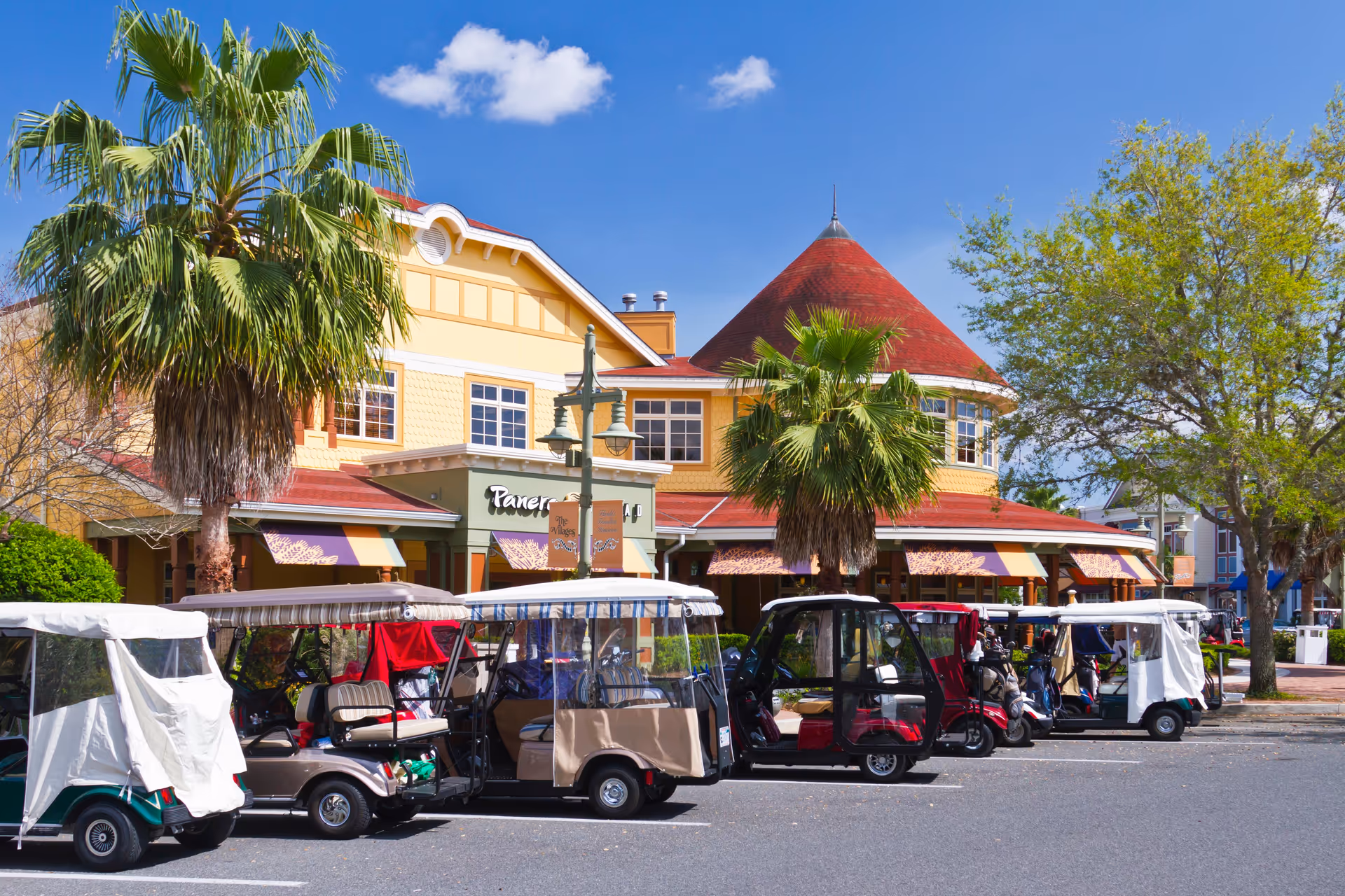 Colorful shopping center building with palm trees and lined-up golf carts in front.