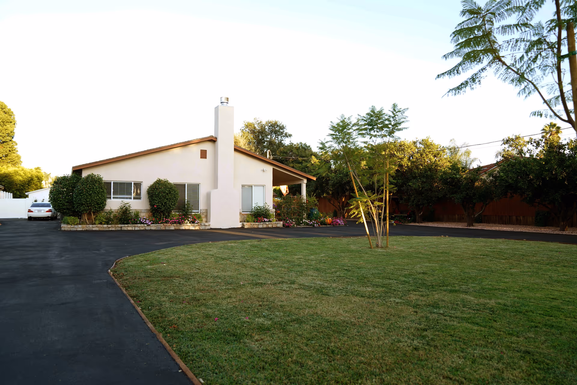 Single-story ranch-style house with a paved driveway, manicured front lawn, and trees.