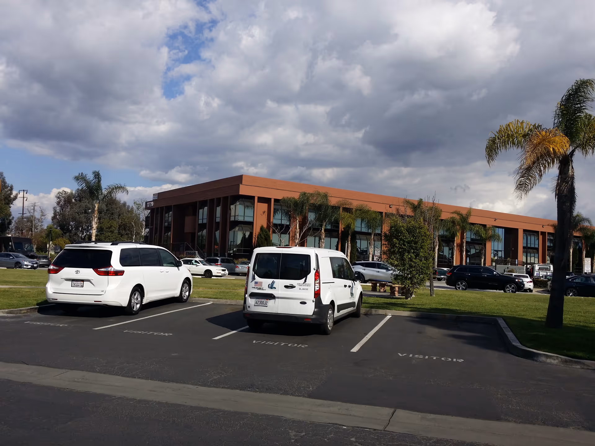 Exterior view of a low-rise brick building with palm trees and parked cars.