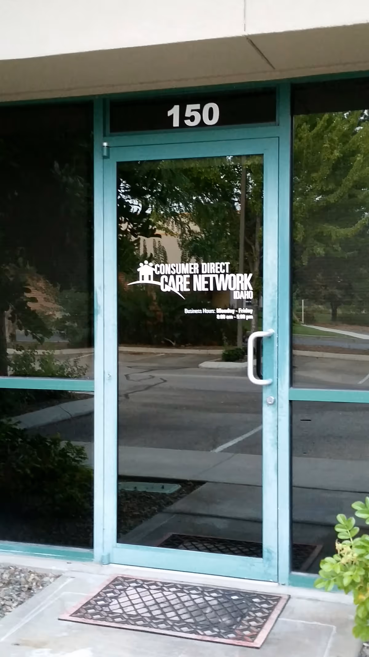 Teal-framed glass entrance door displaying Consumer Direct Care Network Idaho signage, with street reflections.