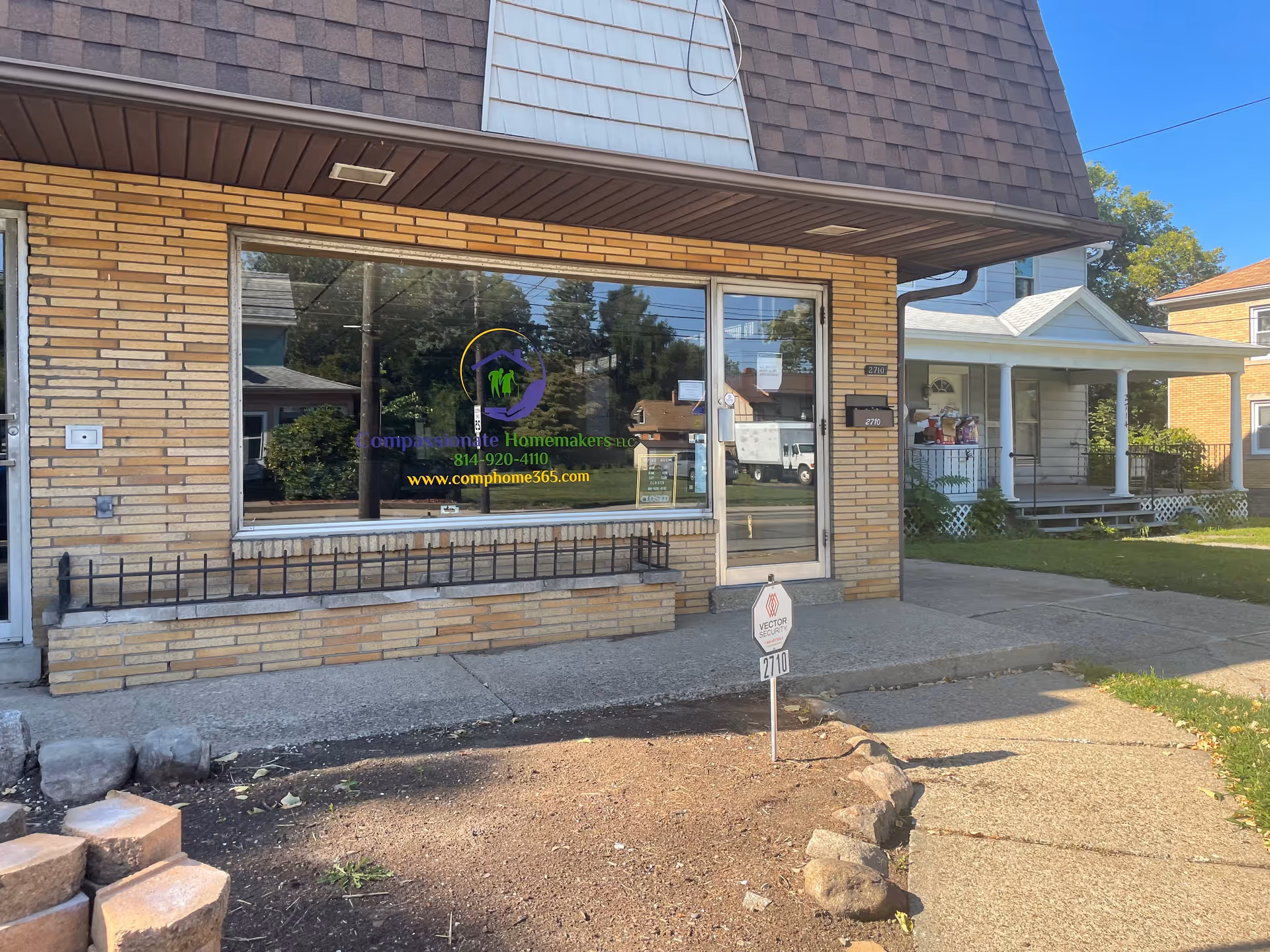 Brick storefront with large front window displaying Compassionate Homemakers logo and contact info.