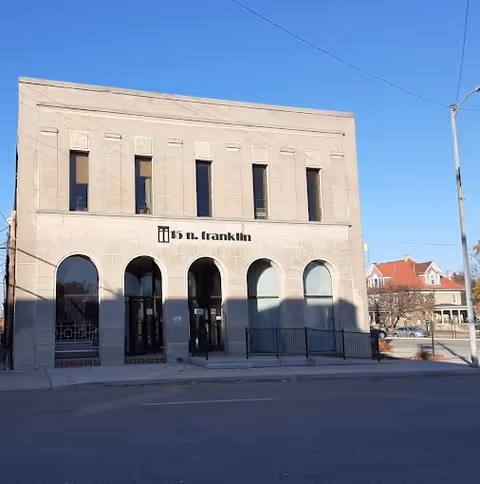 Two-story stone building with arched entryways and a centered sign along the facade.