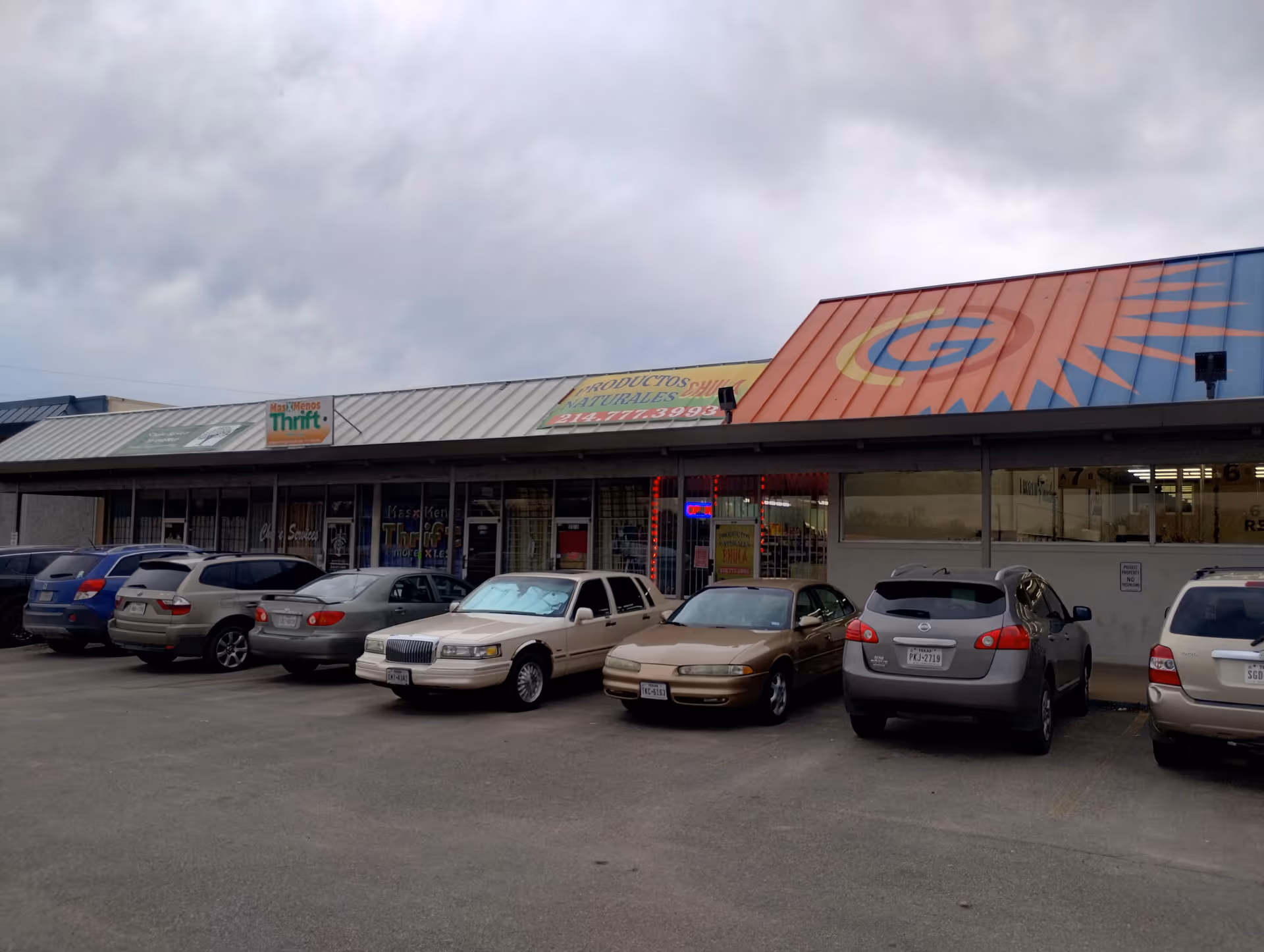 Row of storefronts with parked cars in a strip mall exterior.