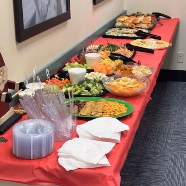 A long buffet table with assorted snacks and fruit on a red tablecloth.