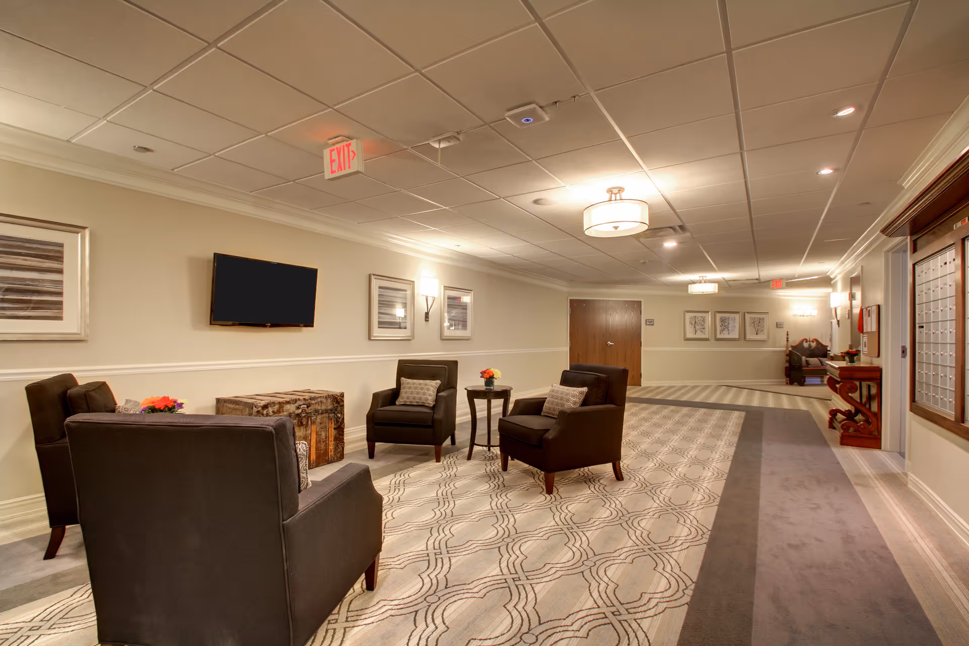 Lobby-style common area with black chairs, a TV, and framed art along a hallway.