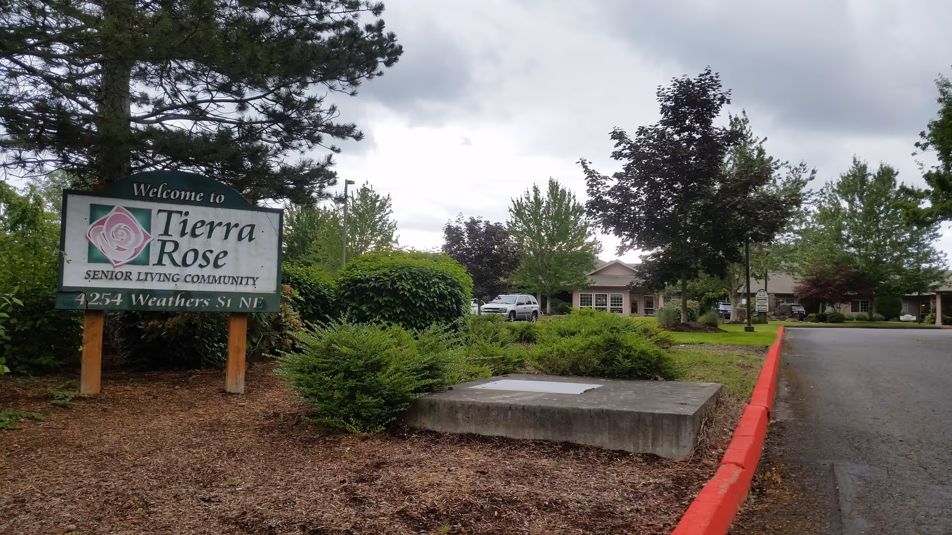 Exterior view of a senior living facility with a sign and landscaping.