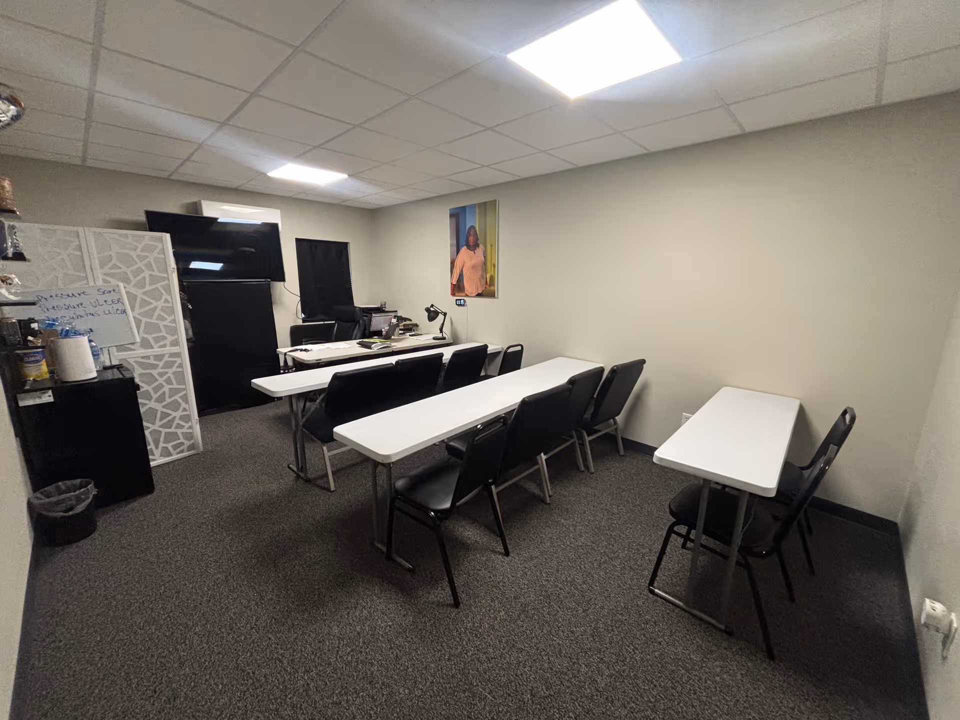 Small multipurpose training room with white tables, black chairs, and a wall-mounted TV.