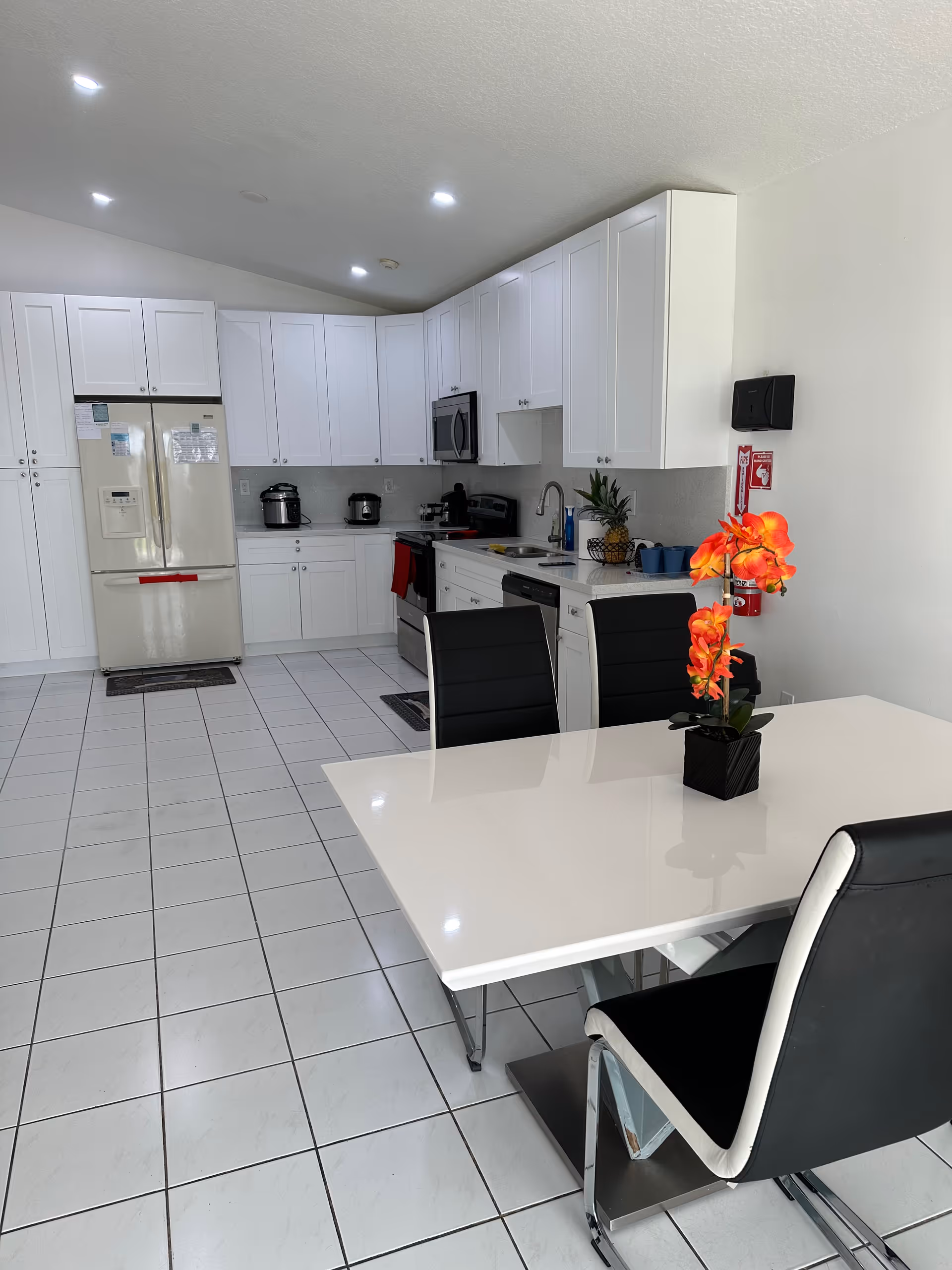 Bright white kitchen with ample cabinets, fridge, and a dining table with orange orchid centerpiece.