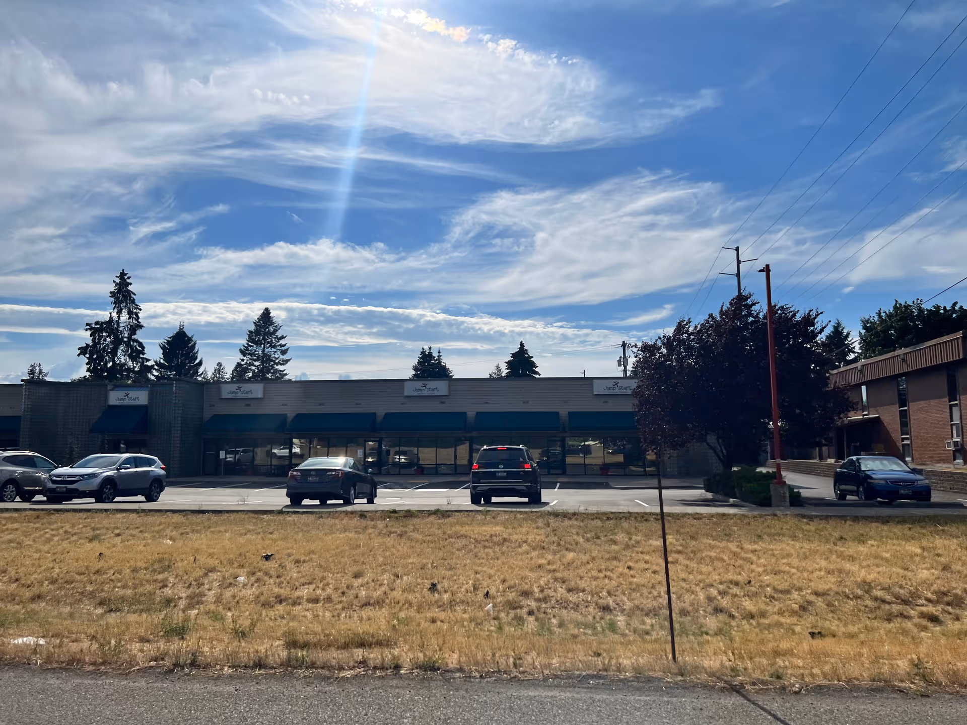 Exterior view of a single-story strip with blue awnings, parking lot, and trees.