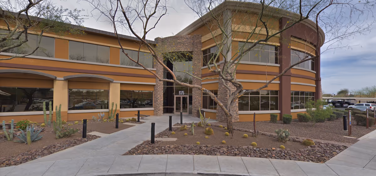 Exterior view of a modern senior living facility with tan walls, large windows, and desert landscaping.