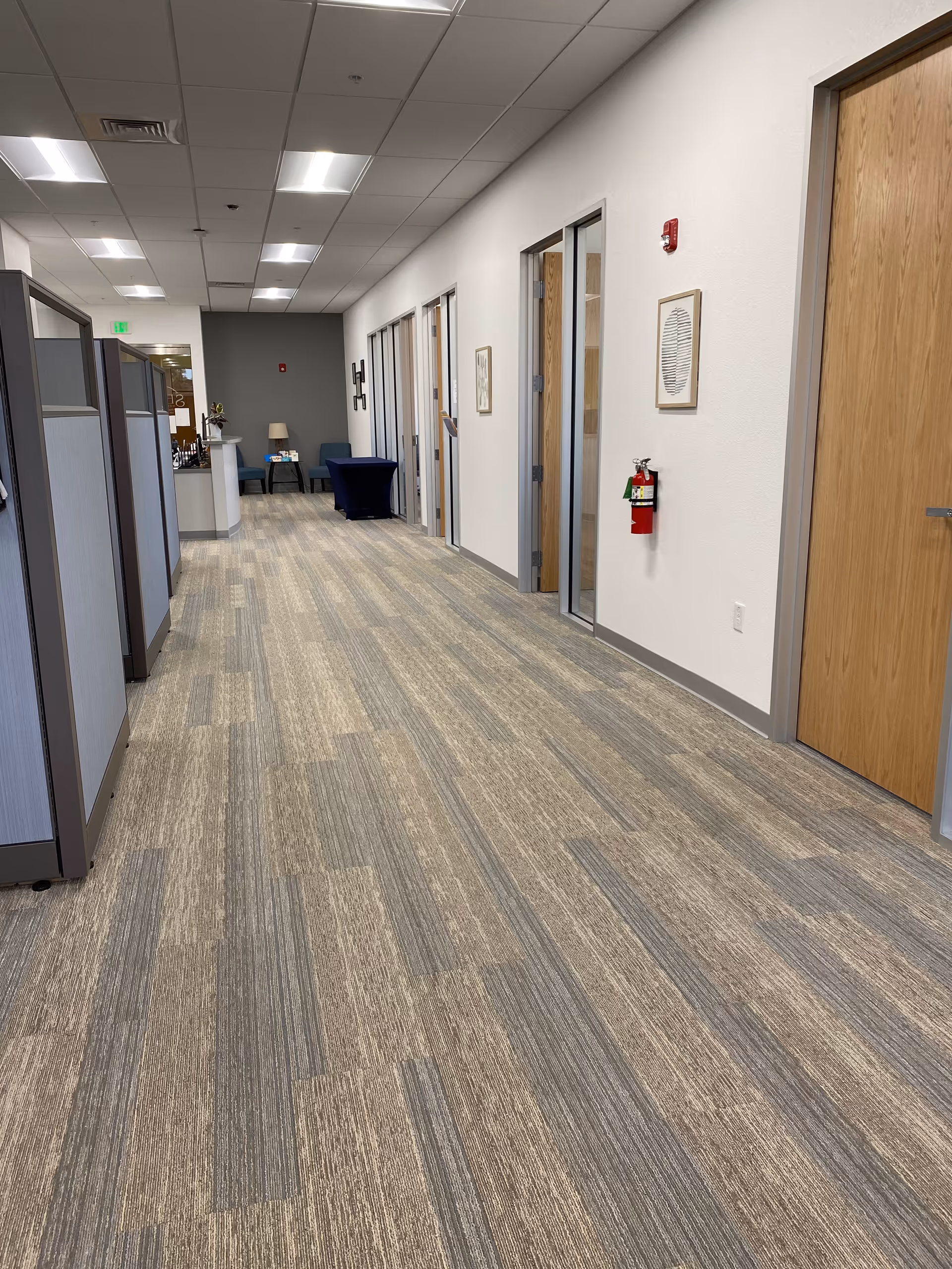 Long interior corridor with cubicles on the left and closed doors along a carpeted hallway.