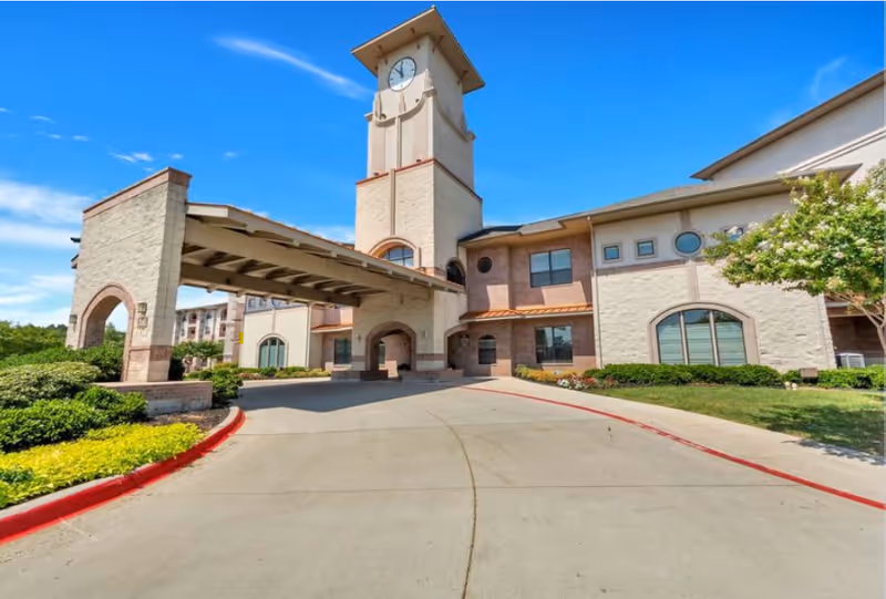 Front entrance of a senior living facility with a covered driveway/porte-cochère and a tall clock tower.