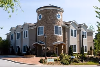 Exterior view of a two-story senior living building with a circular brick tower and landscaped entrance.