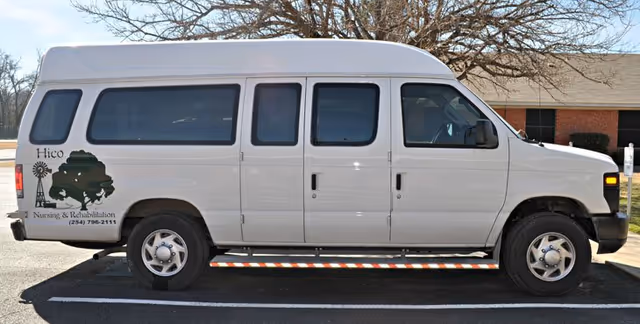 A white van with Hico Nursing and Rehabilitation logo parked beside a brick building.