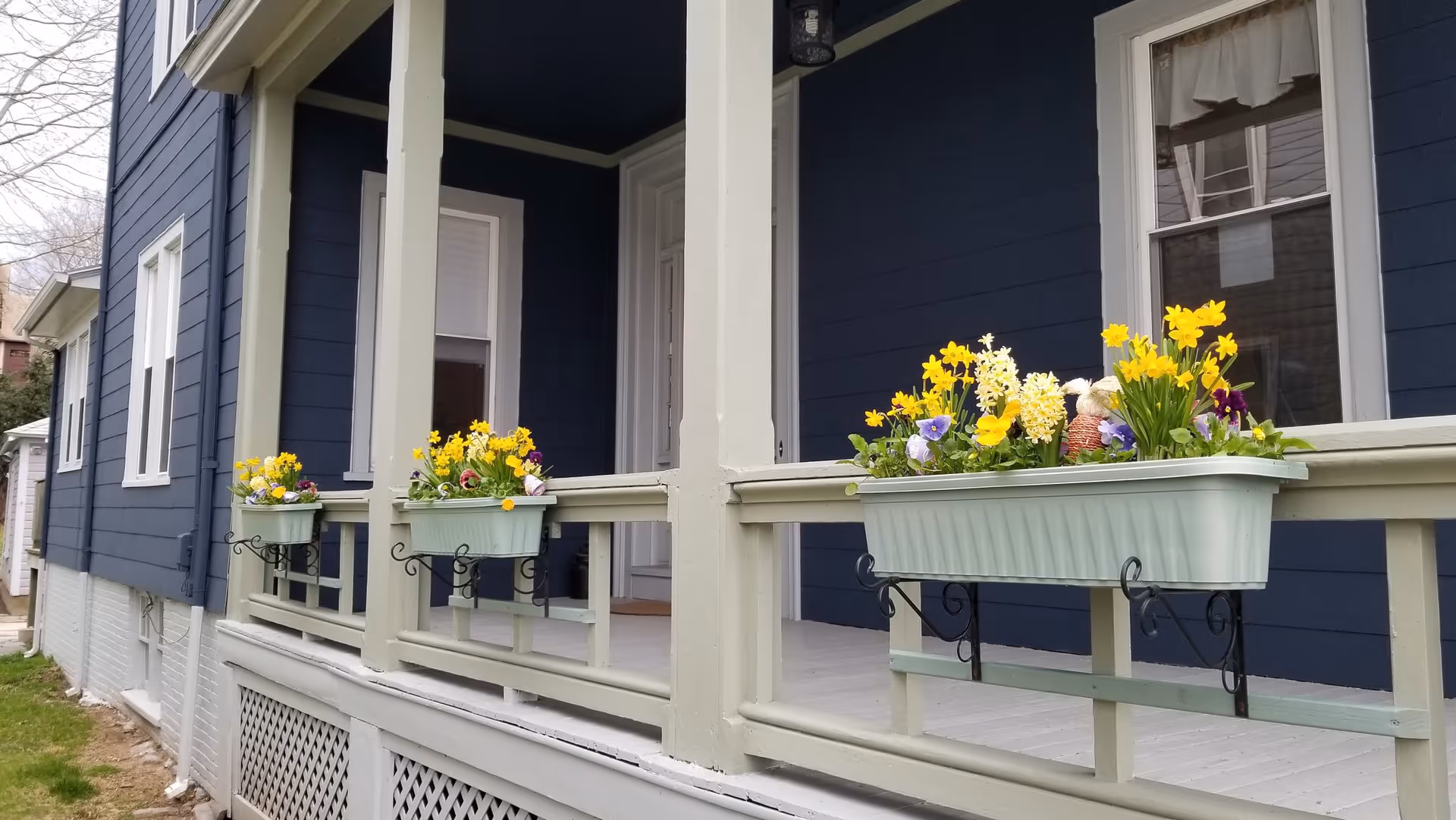 Dark blue building exterior with a covered porch and flower-filled planters along the railing.