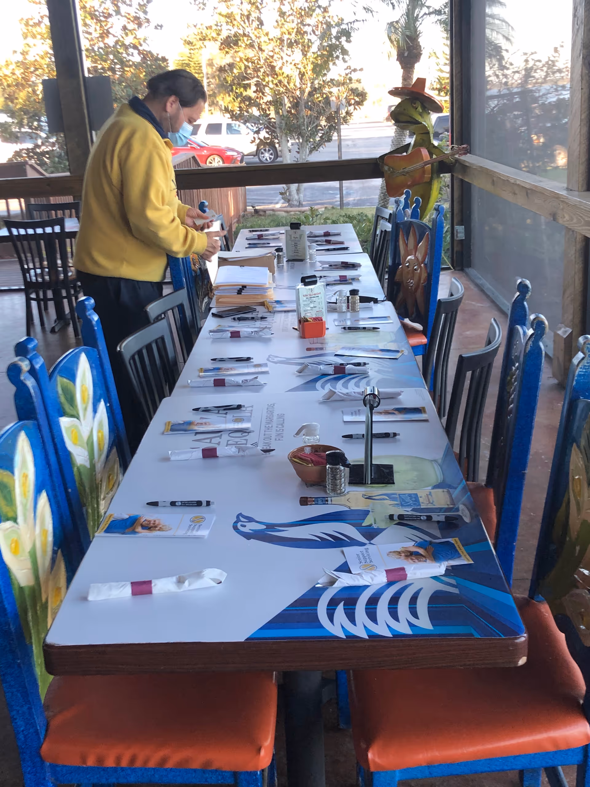 Staff member wearing a mask arranges an outdoor dining table with place settings.