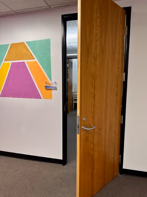 Open wooden door reveals a hallway with colorful abstract wall art.