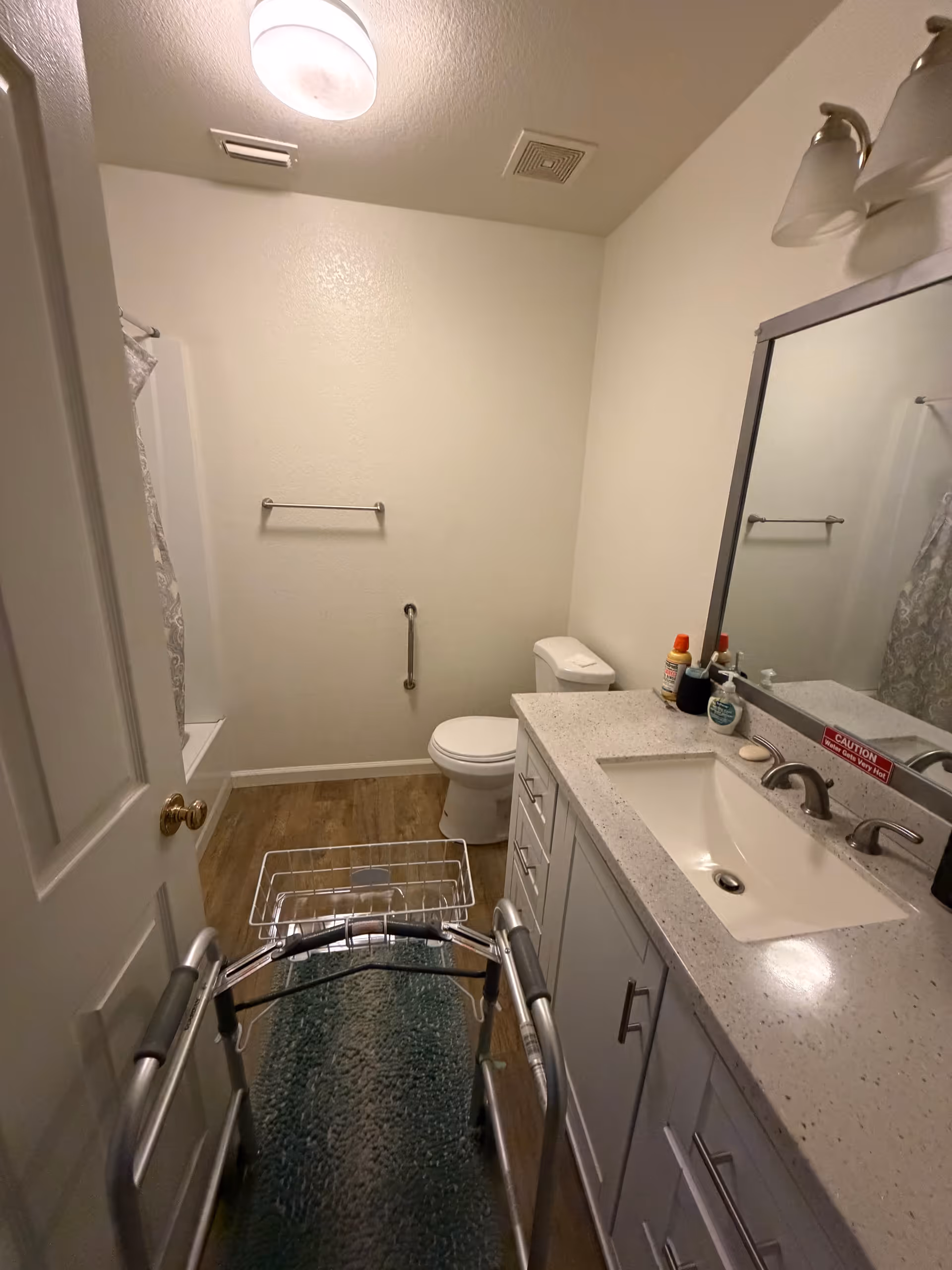 Small bathroom with sink, mirror, toilet, tub, and a walker in front.