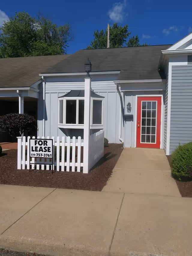 Exterior view of a light-blue facility with a red-framed door and white fence.