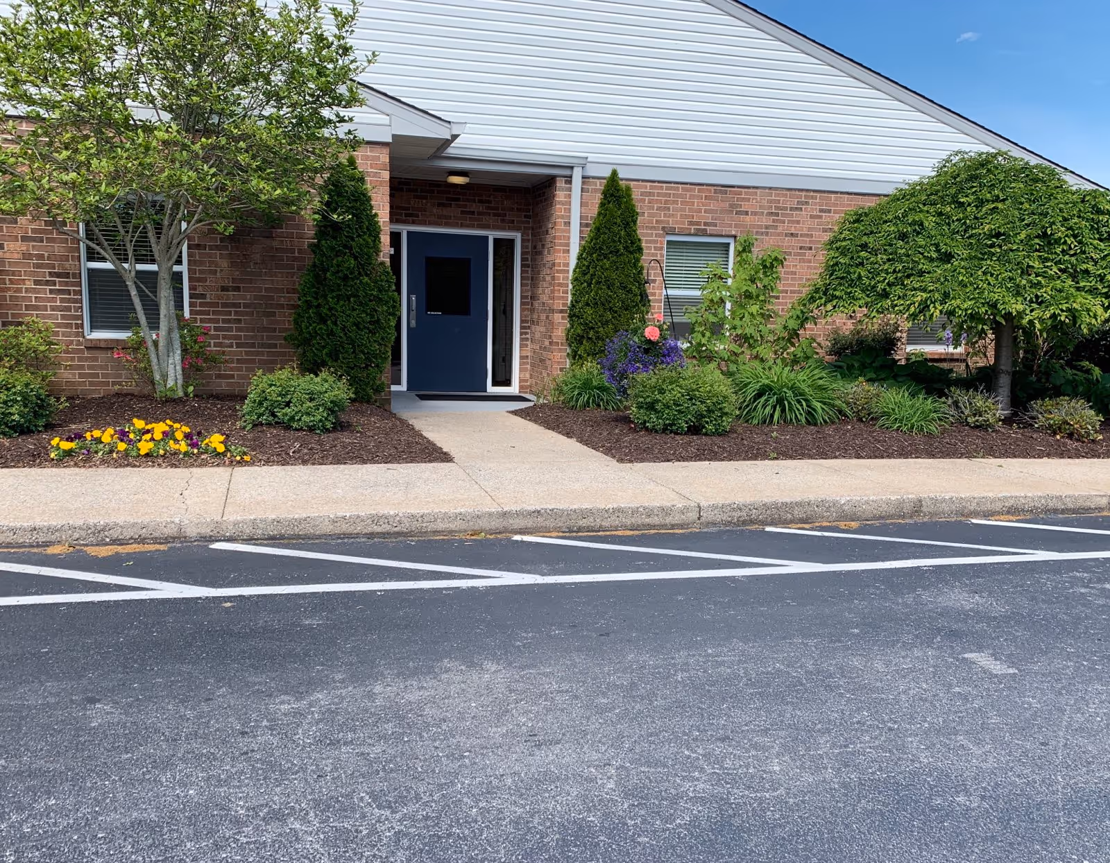 Exterior view of a brick senior living facility entrance with a blue door and landscaping.