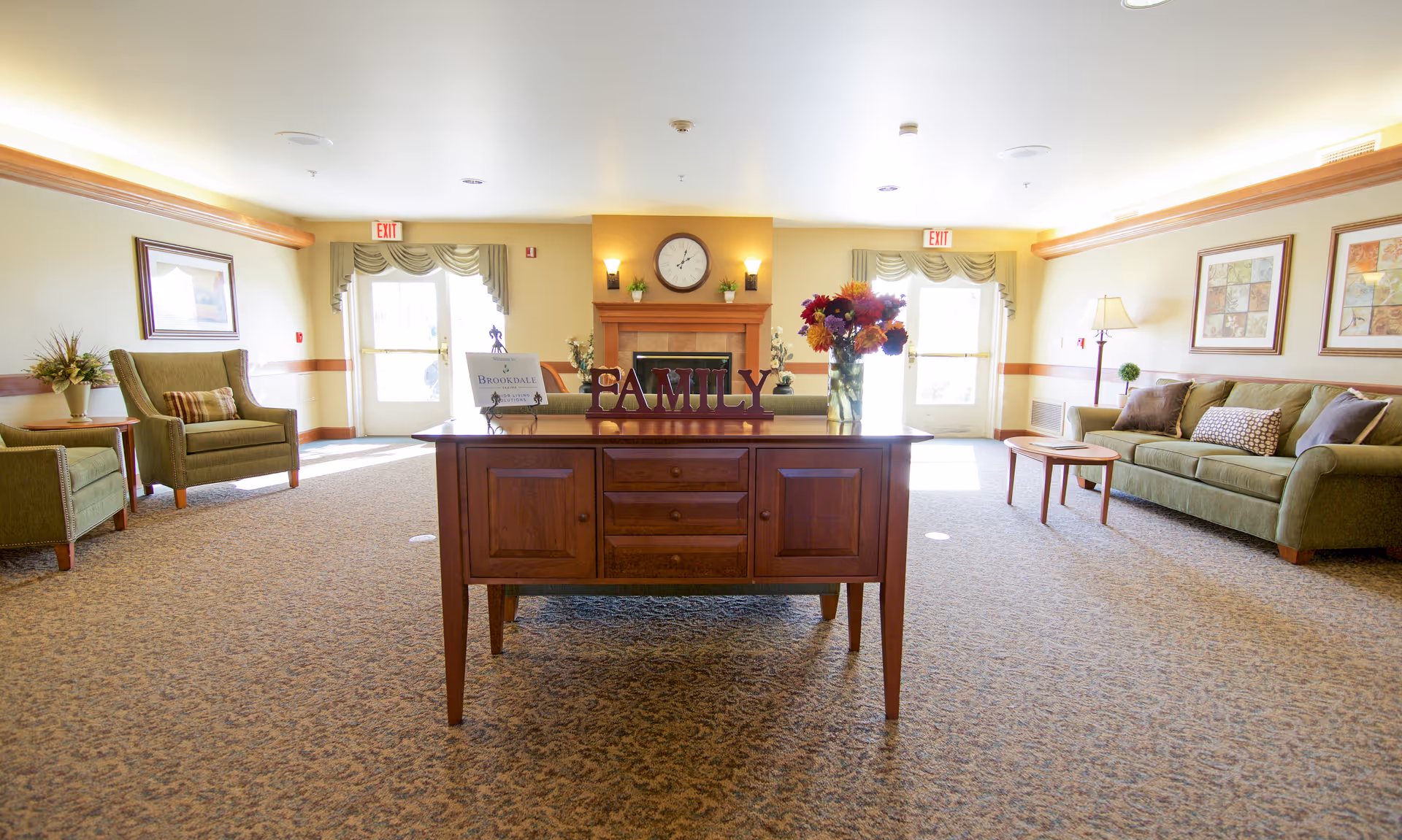 Lobby-style living room with a central wooden console table, sofas, and floral decor.