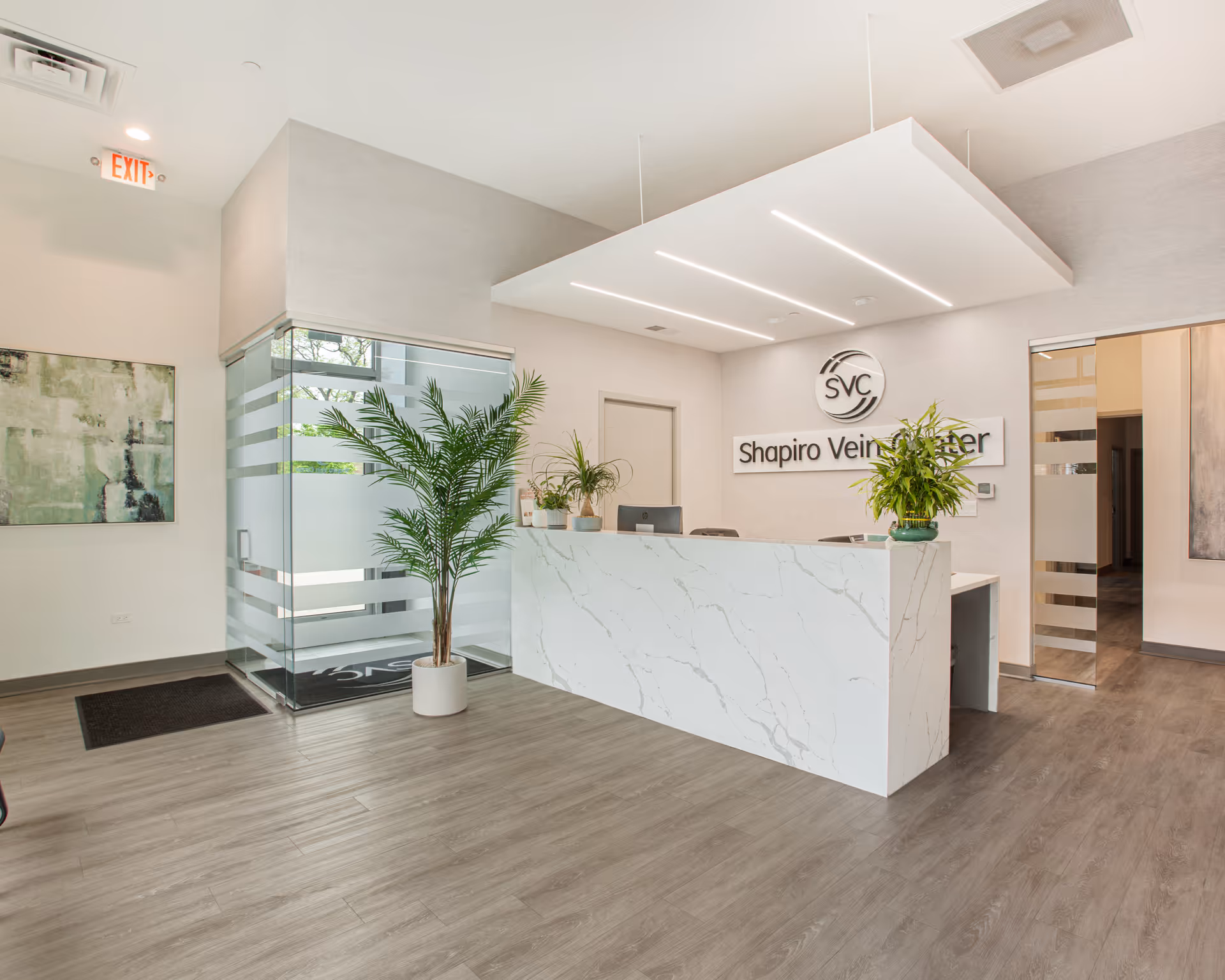 Shapiro Vein Center reception area with marble counter, glass walls, and potted plants.