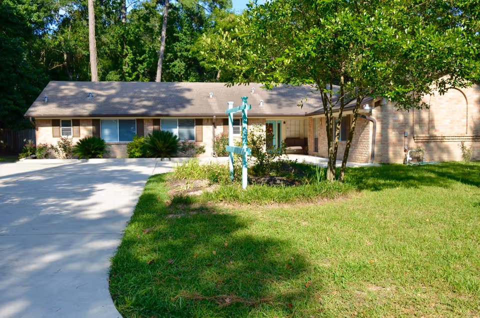 Single-story brick senior living facility with a driveway, front lawn, and trees.