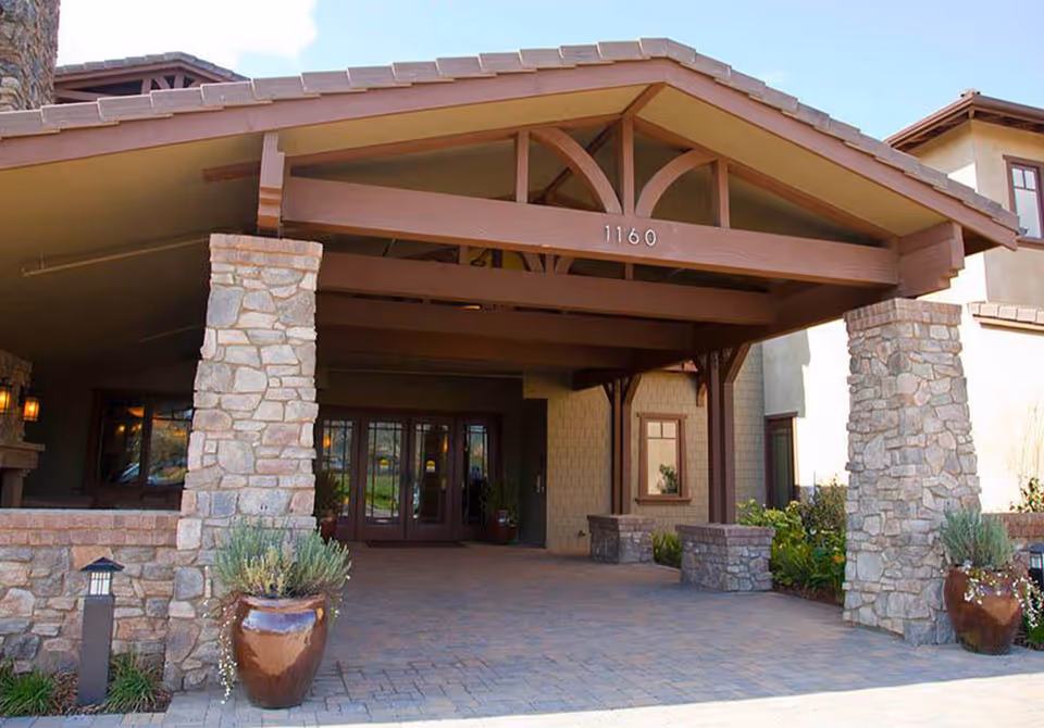 Stone-entry pavilion with wooden beams frames glass doors at Westmont of Morgan Hill.
