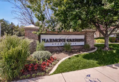 Exterior view of Harmony Gardens Apartments sign with landscaped entrance.