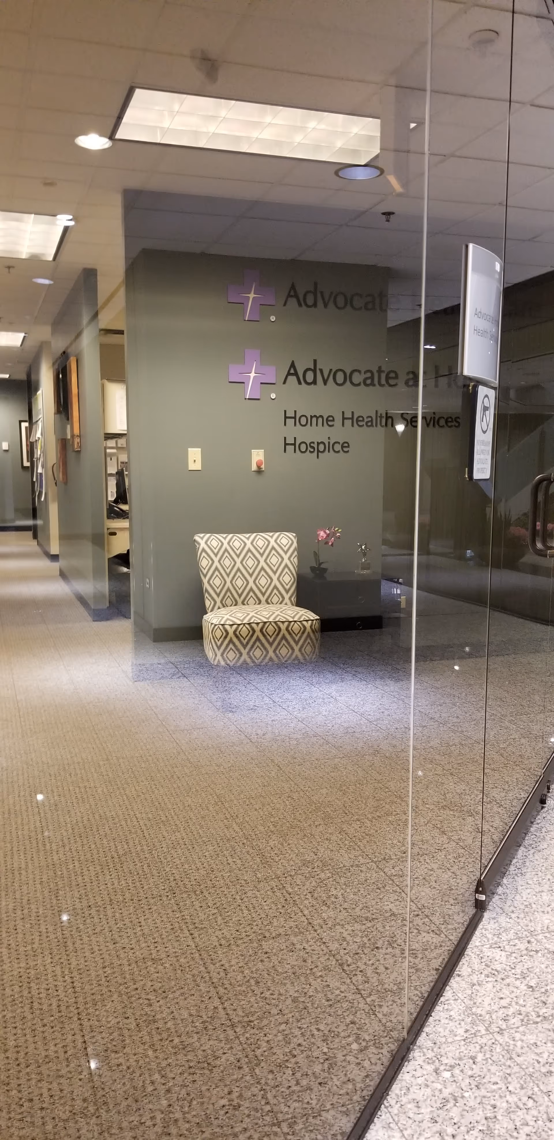 Interior lobby with glass walls, a patterned chair, and Advocate at Home signage.