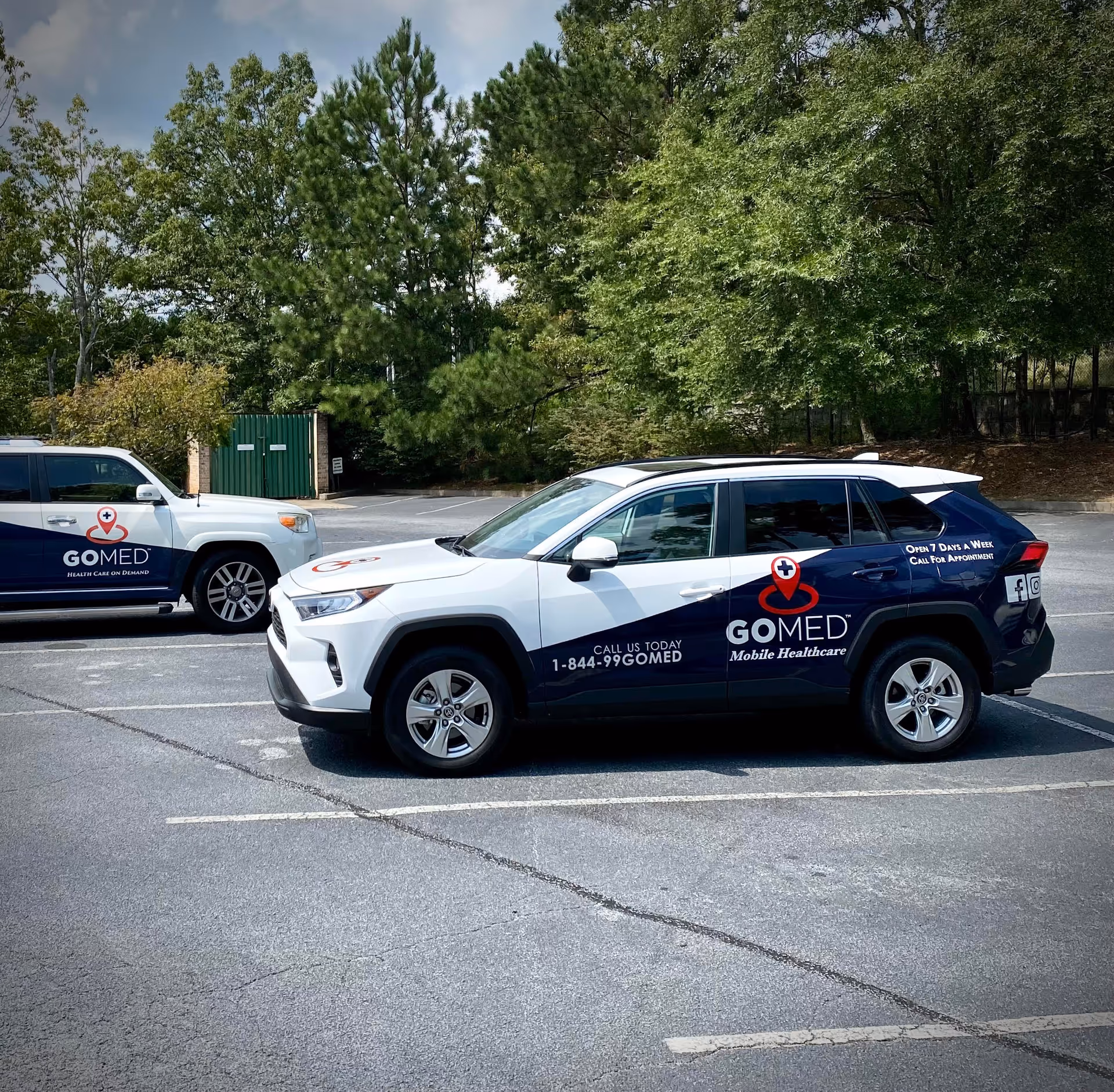Two GOMED Mobile Urgent Care vehicles parked in a lot with trees behind.