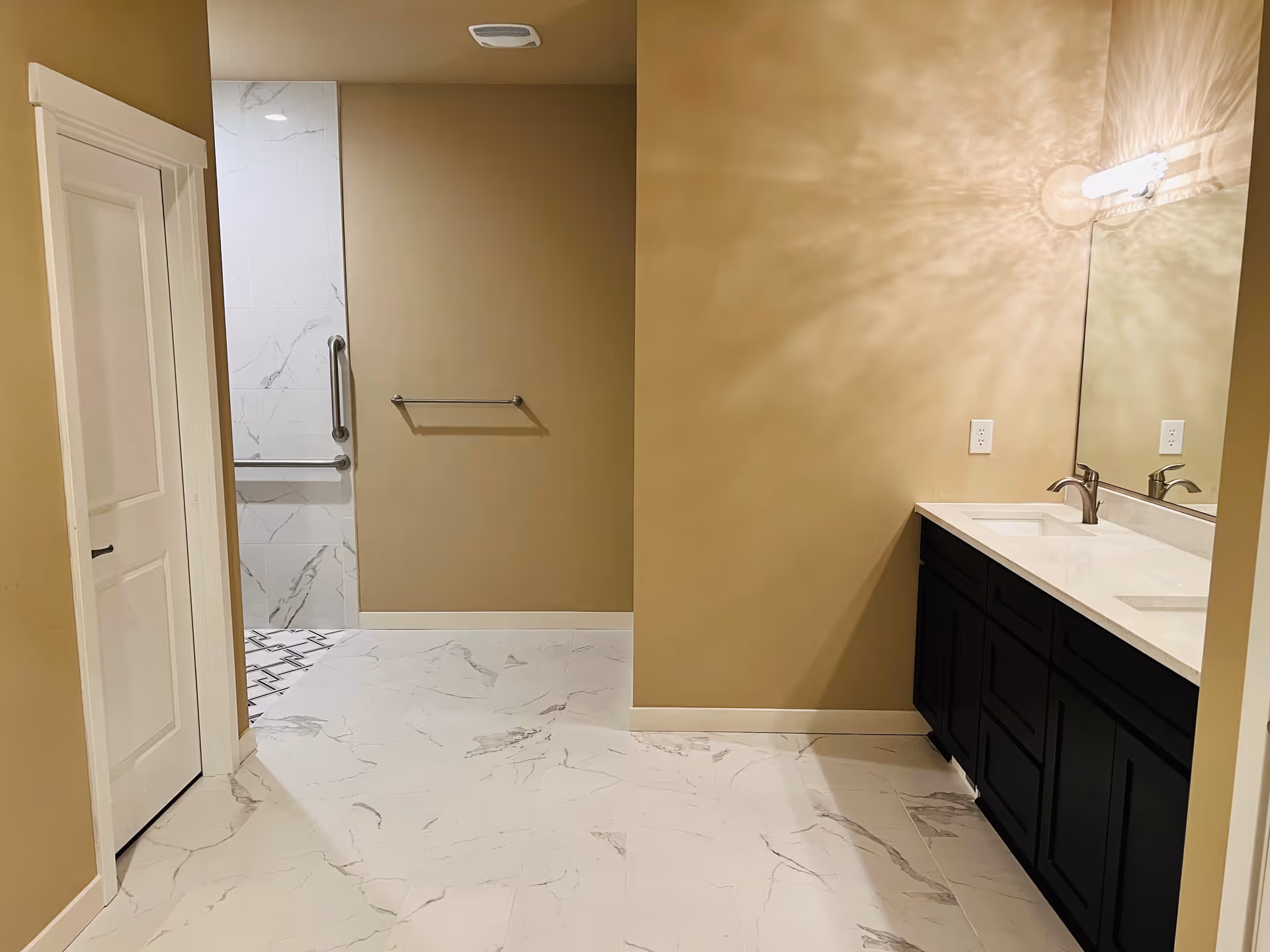 Clean bathroom with marble tiles, beige walls, double sink vanity, and accessible shower.