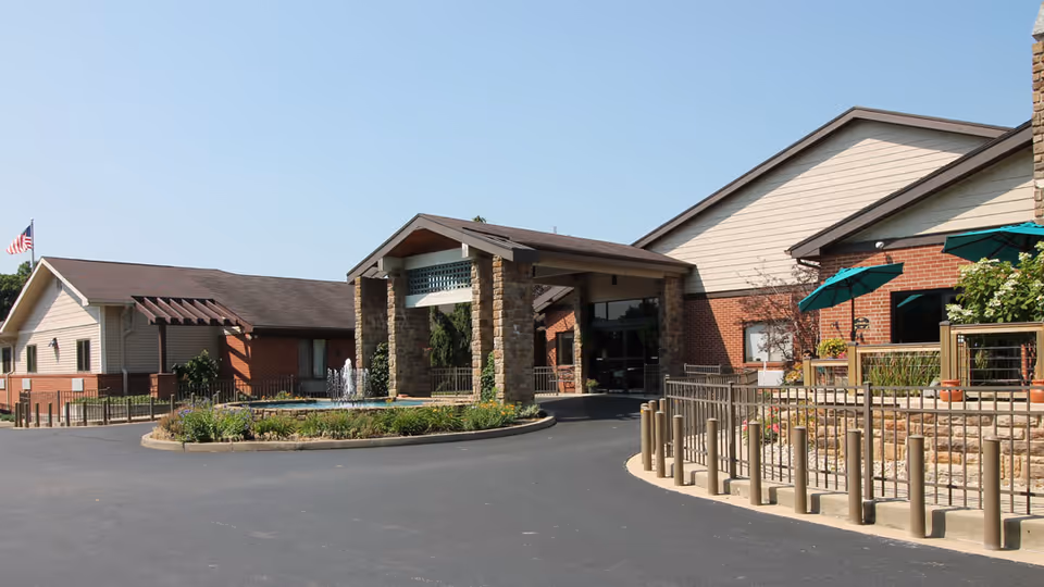 Front entrance of SEM Haven senior living facility featuring a covered porte-cochere, circular driveway, fountain, patio umbrellas, and landscaped beds.