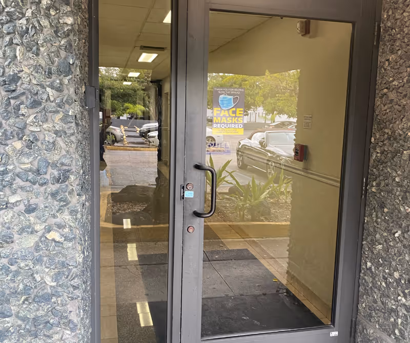 Glass entry door with stone exterior wall and a 'Face Masks Required' sign visible inside.
