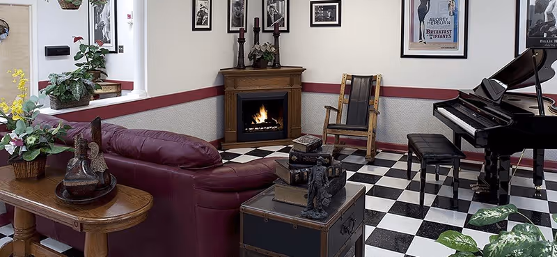 Cozy living room lobby area with checkered floor, fireplace, piano, and seating.