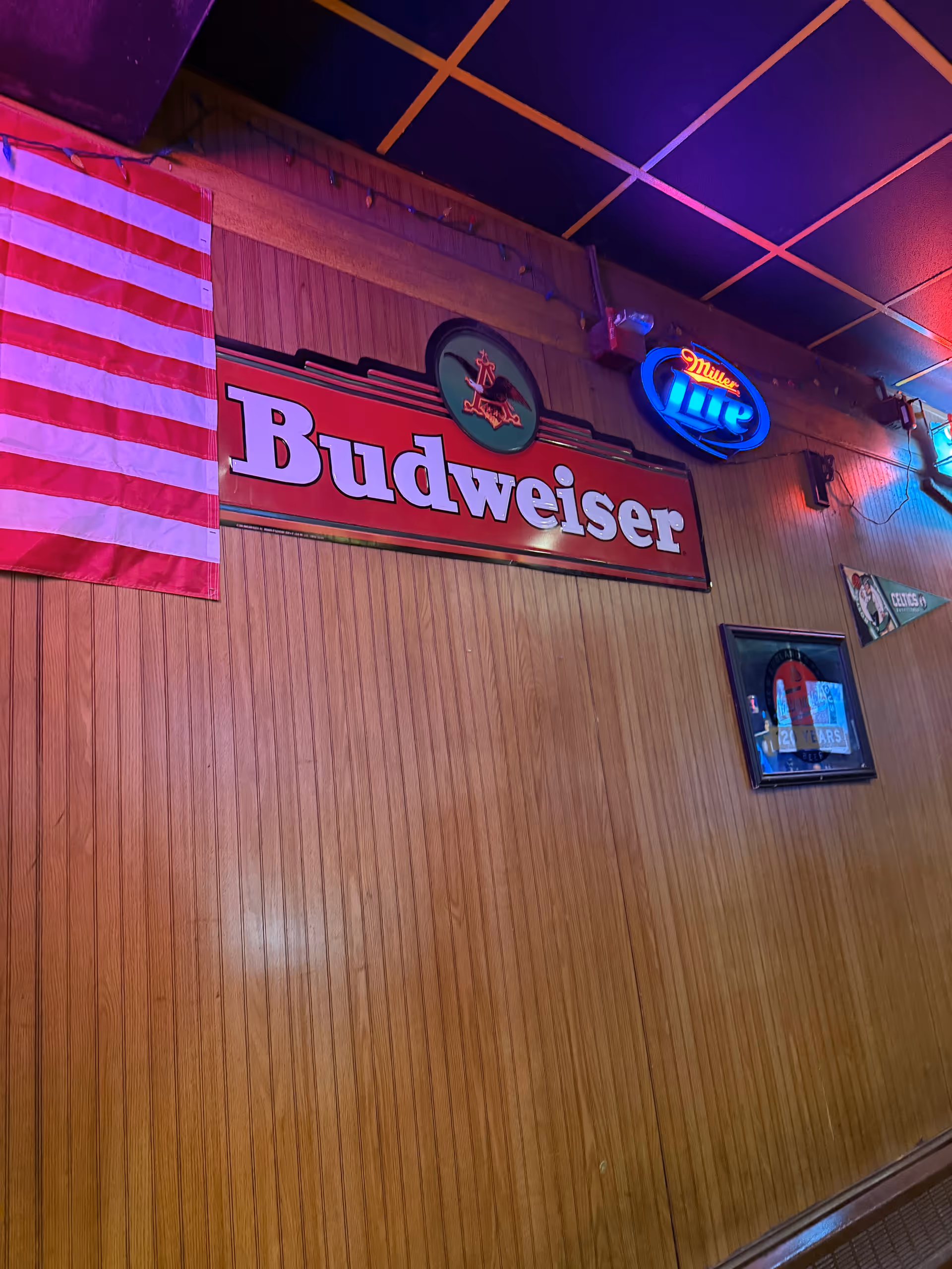 Wood-paneled interior with American flag and Budweiser sign above a bar.