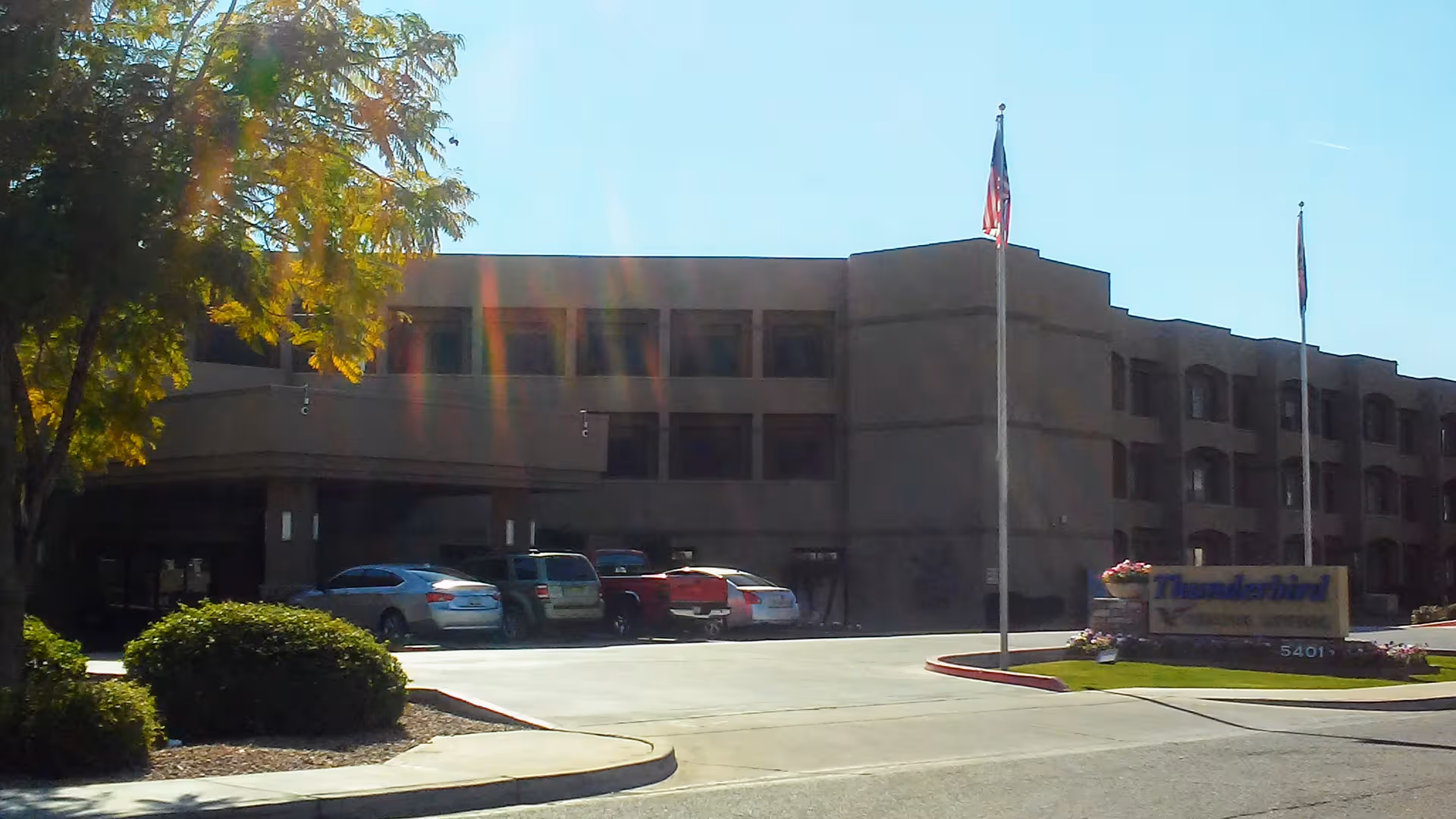 Exterior view of Thunderbird Senior Living building with parked cars and flagpoles
