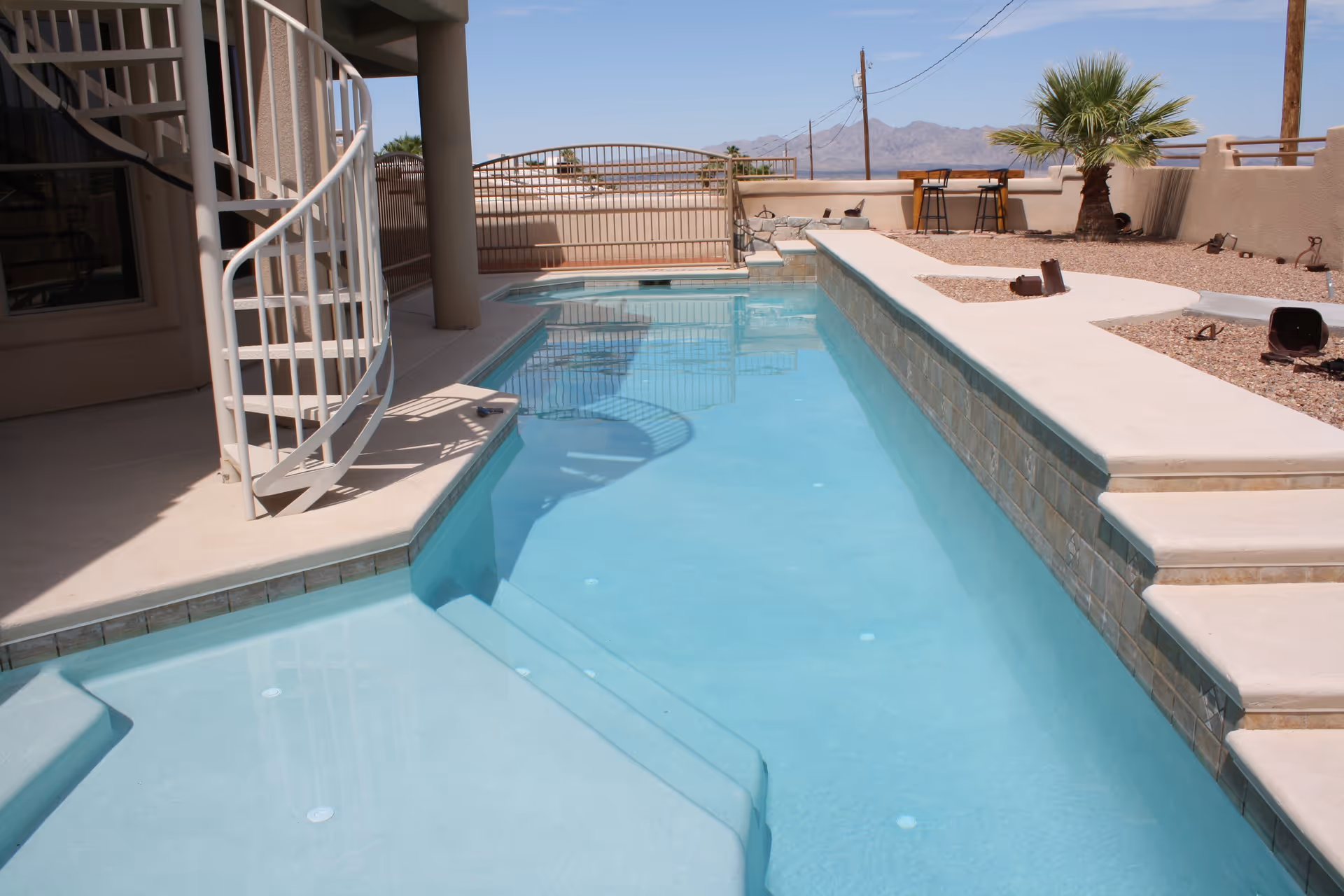 Outdoor pool area with steps, beige decking, and desert landscape under clear sky.
