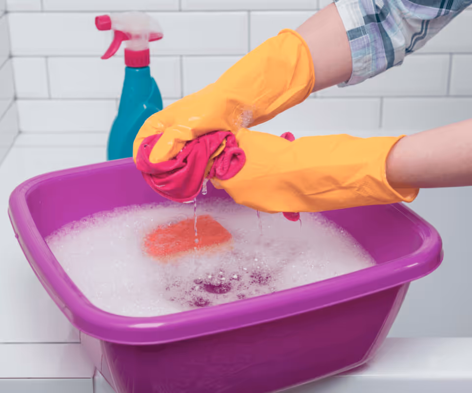 Person wearing yellow gloves washes items in a purple tub of soapy water.