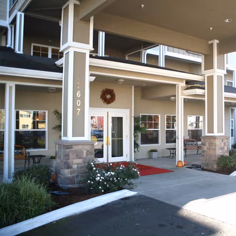 Front entrance of a senior living building with a covered portico, columns, double glass doors, a wreath and a red welcome mat.