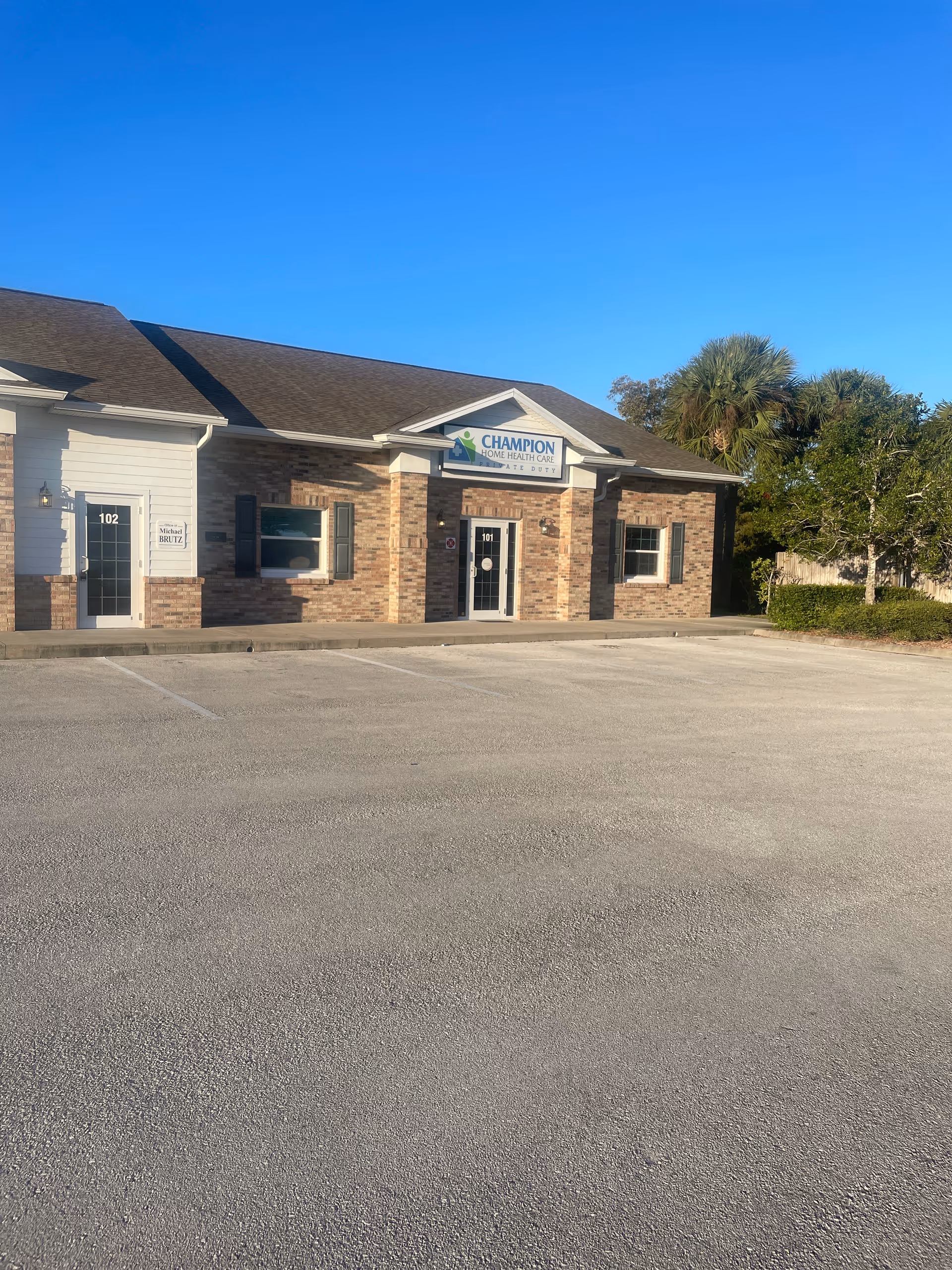 A single-story brick building labeled Champion Home Health Care, with a parking lot in front.