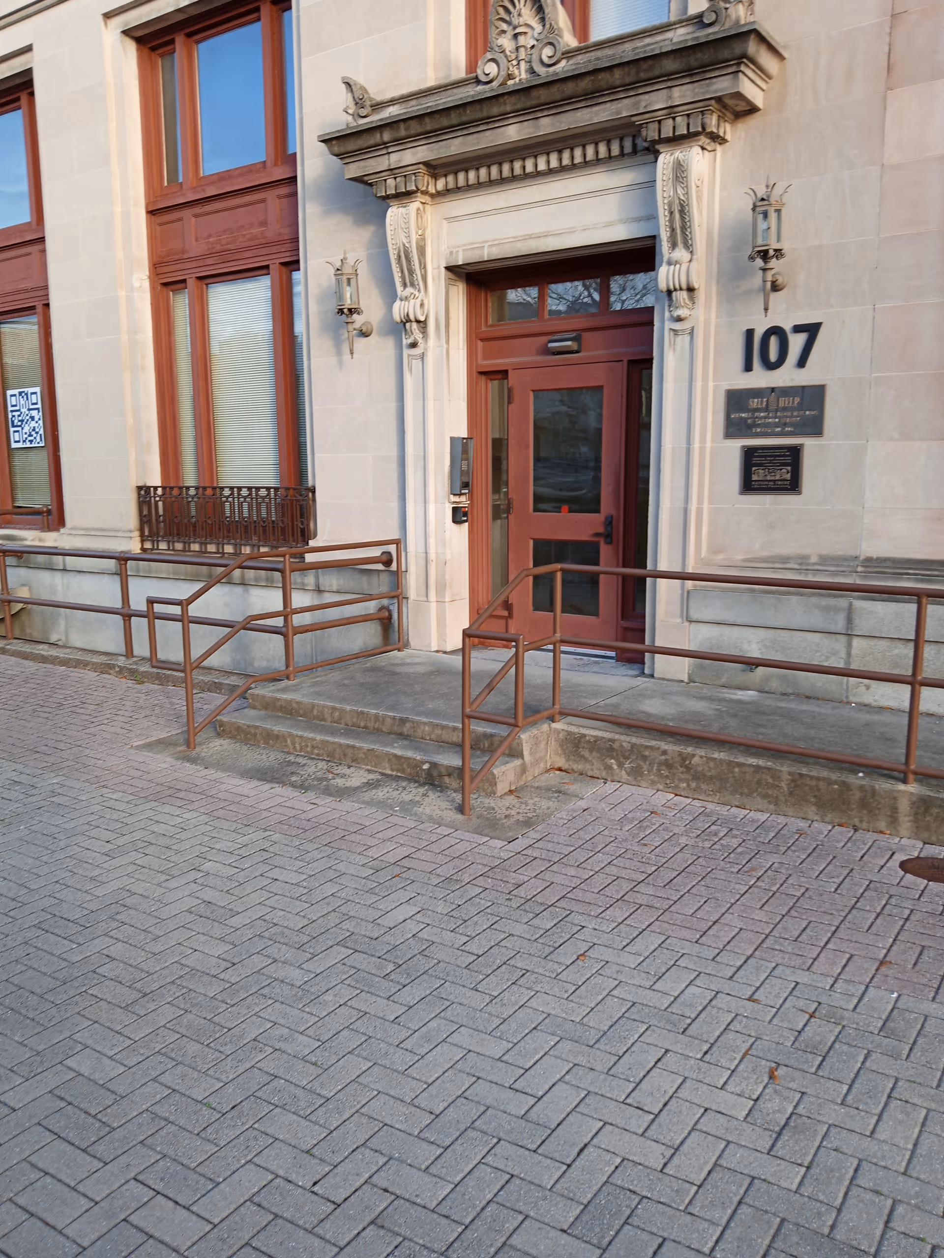 Exterior view of a stone building entrance with steps, rails, and a red door