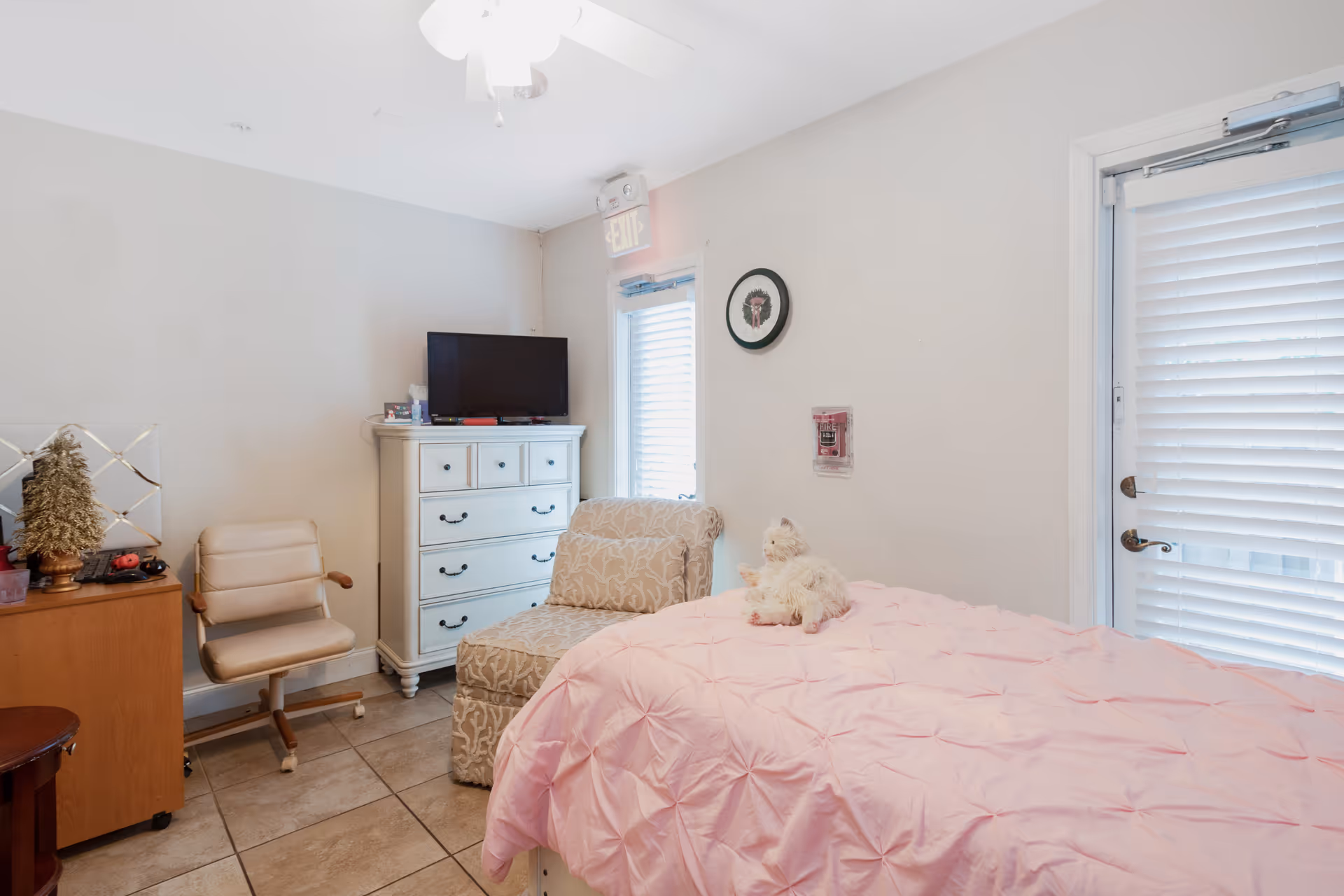 Bright bedroom with a pink quilted bed, white dresser, and TV in a cozy corner.
