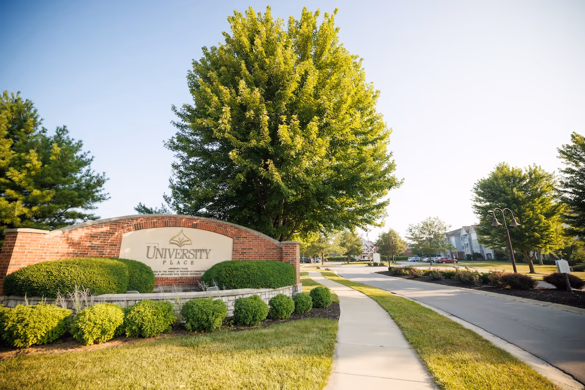 A brick entrance sign for University Place surrounded by trimmed shrubs and trees.
