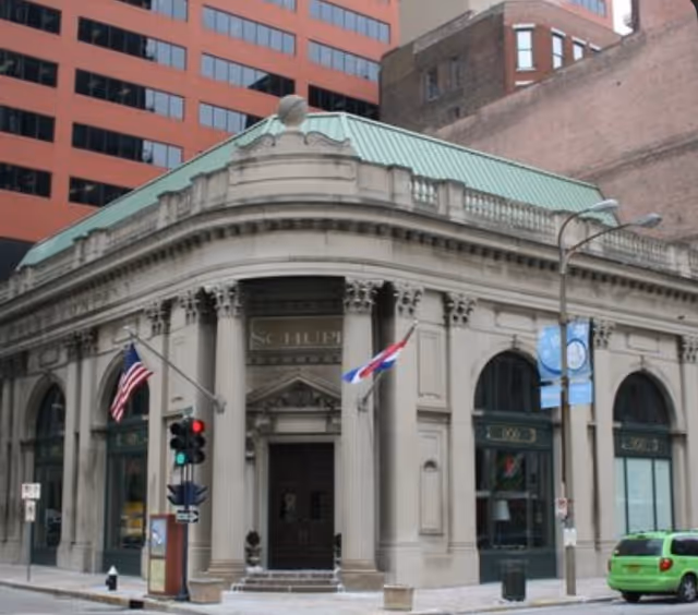 Historic stone building with columns, arched windows, and flags on a city street.