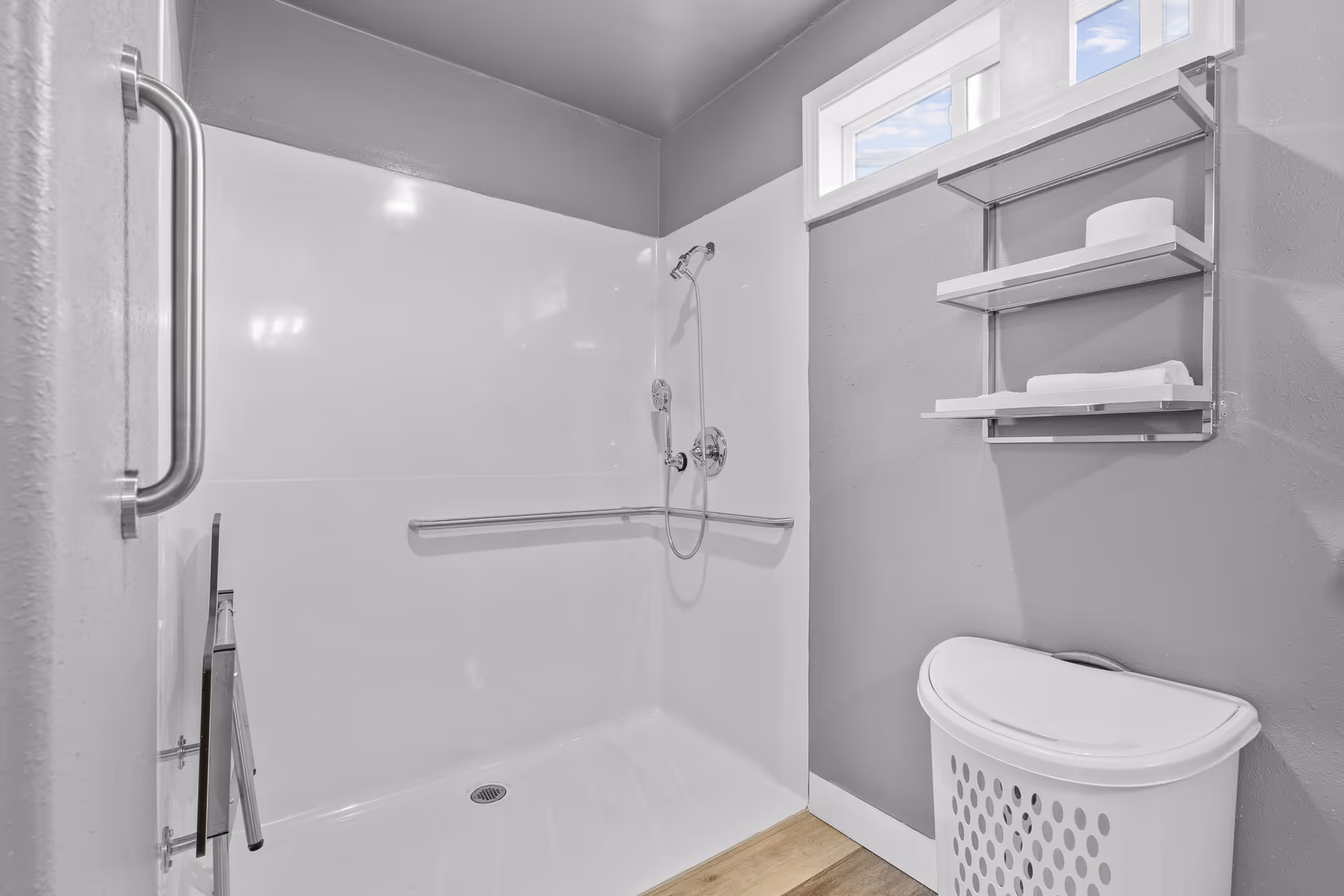Accessible bathroom featuring walk-in shower, grab bars, shelving, and a laundry basket.