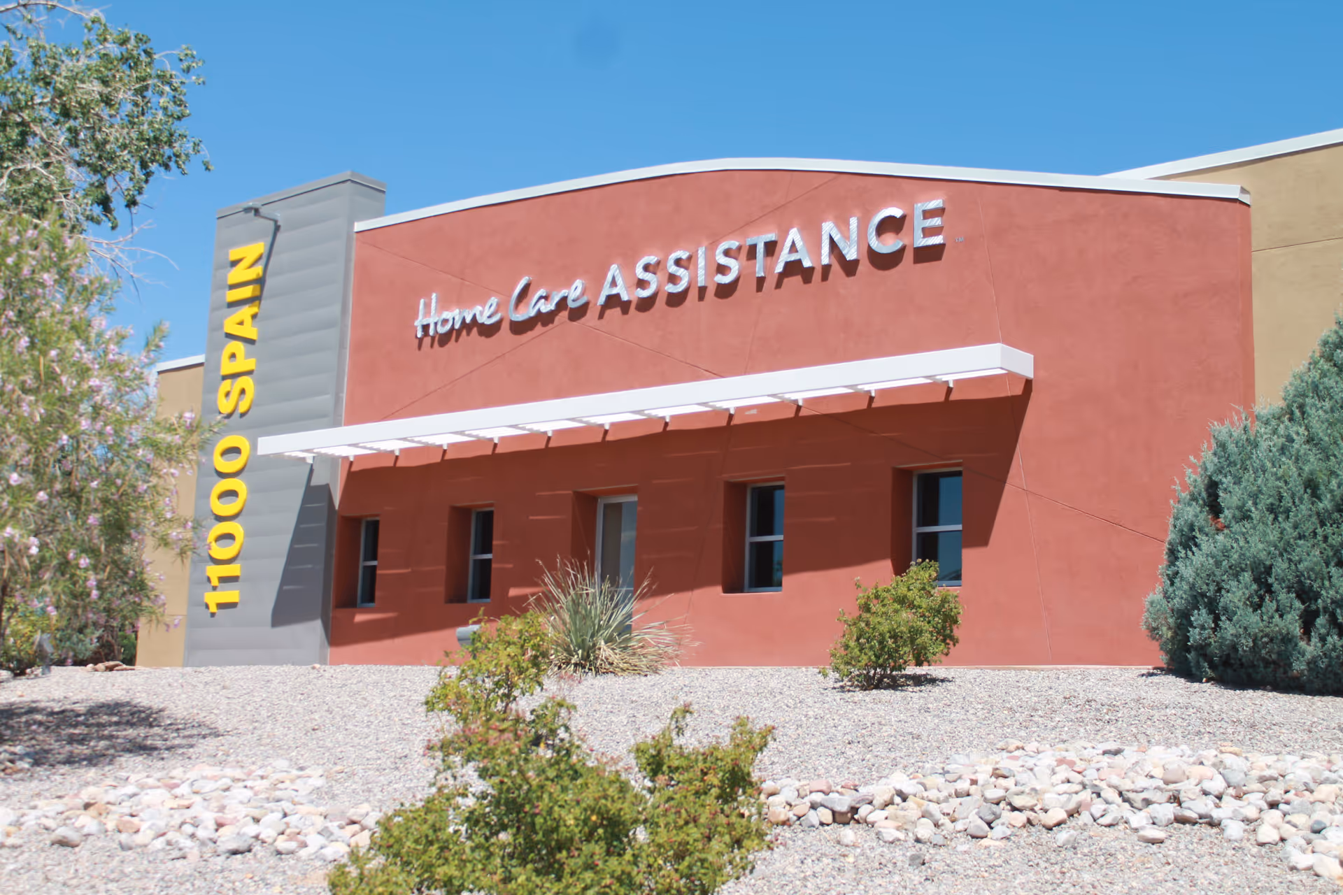 Exterior of a red Home Care Assistance building with desert landscaping and signage.