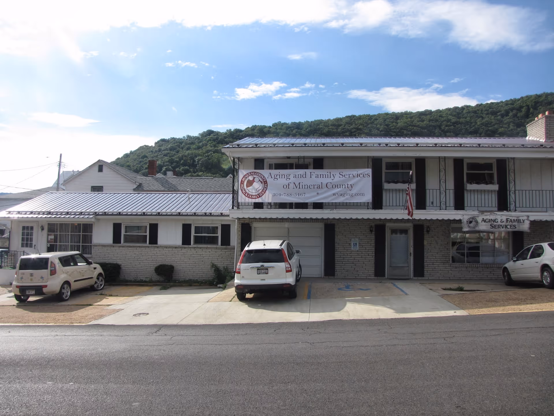 Exterior of Aging & Family Services building with sign and parked cars.