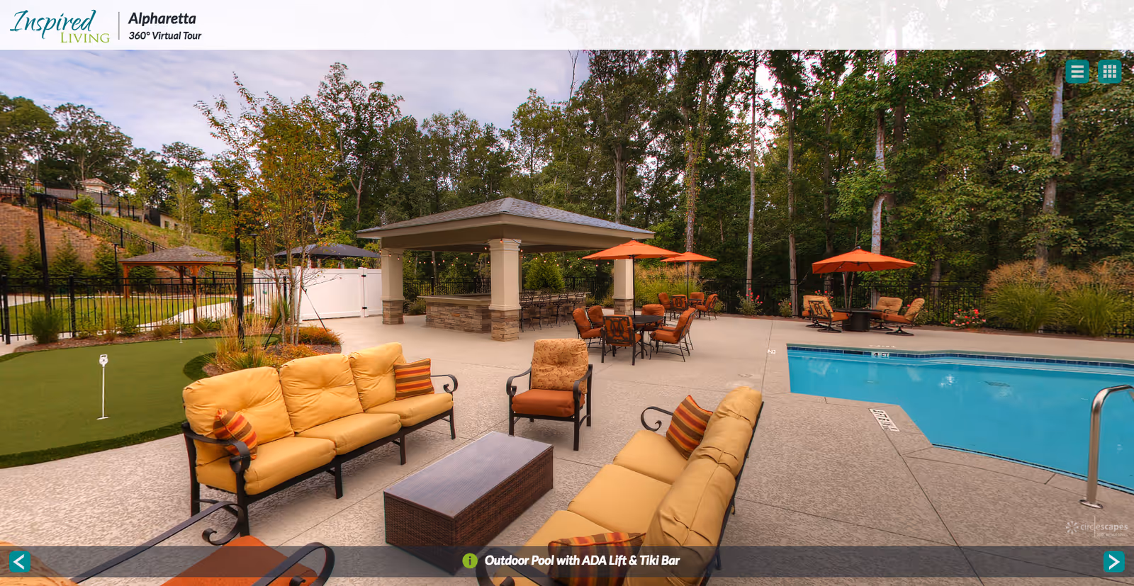 Outdoor seating area with cushioned chairs and sofas around a coffee table near a swimming pool. There are several tables with orange umbrellas and chairs, a tiki bar under a pavilion, and a small putting green. The area is surrounded by trees and landscaping.
