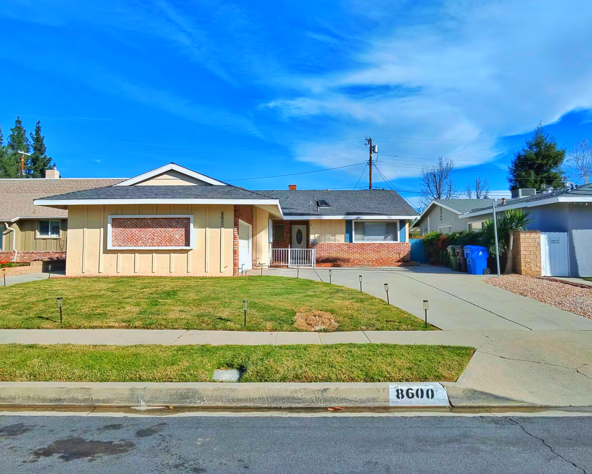 A single-story suburban house with a front lawn, driveway, and curb.